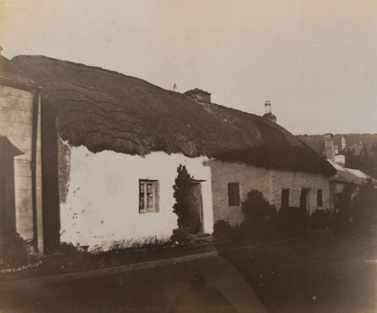 Llun du a gwyn yn dangos rhes o fythynnod bach â thoeau gwellt.