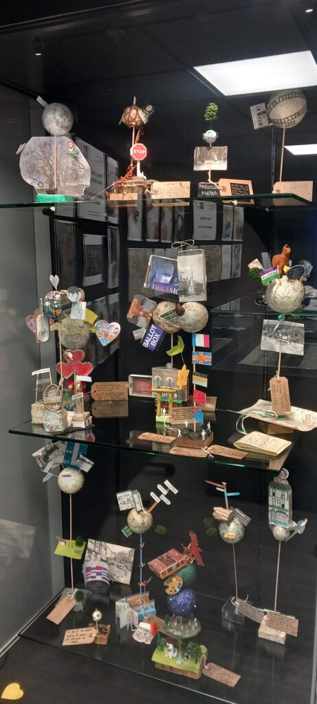 A glass display case filled with small, handcrafted dioramas and miniature models arranged on multiple shelves.